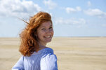 smiling-teenage-girl-looking-over-shoulder-while-standing-at-beach-against-sky-on-sunny-day-LB...jpg